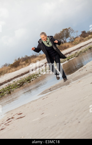 Beautiful senior Woman herumtollen am Strand schreitende zusammen mit ausgebreiteten Armen und einem Lächeln der Wertschätzung, wie sie Natur und die Freiheit von ihrem Ruhestand genießt Stockfoto