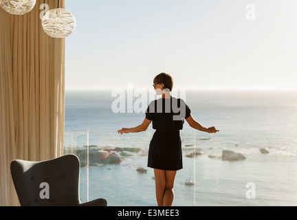 Frau stehend am Balkongeländer mit Blick auf Meer Stockfoto