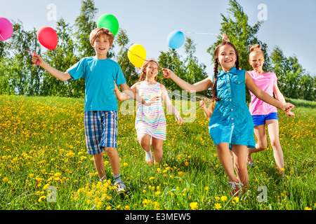 Glückliche Kinder laufen mit Luftballons in grünen Wiese Stockfoto