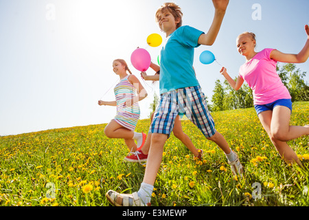 Glückliche Kinder mit Luftballons laufen im grünen Bereich Stockfoto