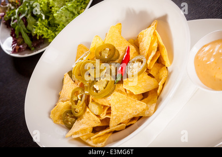 Schüssel mit knusprig goldene Mais Nachos mit Käse-Sauce oder Dip und Oliven als Vorspeise oder zu einer Mahlzeit Vorspeise serviert Stockfoto