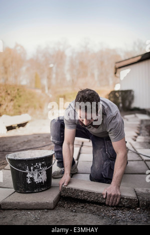 Männliche Zimmermann Positionierung Naturstein Fliesen in Hof Stockfoto