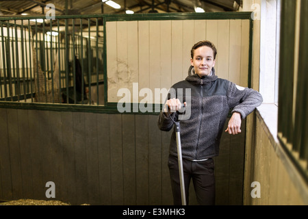 Porträt von zuversichtlich junger Mann mit Heugabel im Pferdestall Stockfoto