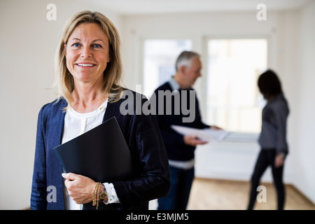 Porträt von zuversichtlich Immobilienmakler mit Kollegen und Frau im Hintergrund zu Hause Stockfoto