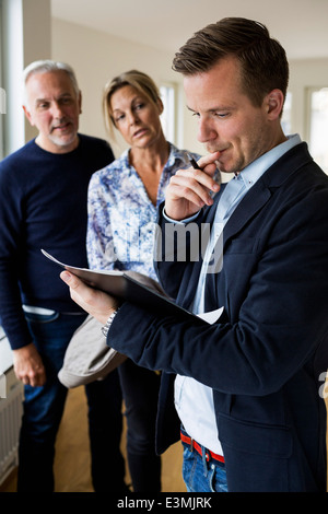 Männliche Immobilienmakler Vereinbarung mit paar stehen im Hintergrund zu Hause lesen Stockfoto