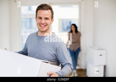 Porträt von glücklichen Menschen tragen Umzugskarton mit Frau im Hintergrund zu Hause Stockfoto