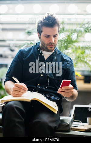 Mitte adult Geschäftsmann mit Handy während des Schreibens in Buch im café Stockfoto