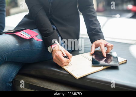 Mittelteil der Geschäftsfrau mit digital-Tablette während des Schreibens in Buch im café Stockfoto