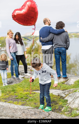 Junge Ballon auf Felsen mit Homosexuellen Familien im Hintergrund halten Stockfoto