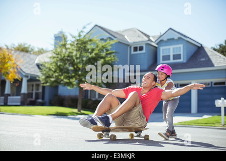 Tochter drängen Vater auf skateboard Stockfoto