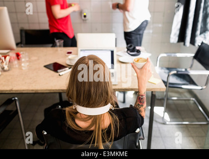 Rückansicht des junge Geschäftsfrau Kaffeetrinken mit männlichen Kollegen im Hintergrund im neuen Büro Stockfoto