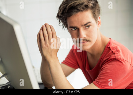 Nachdenklicher junger Geschäftsmann mit den Händen umklammert Computer Schreibtisch im neuen Büro Stockfoto