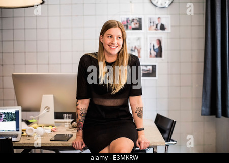 Lächelnde junge Geschäftsfrau lehnt sich am Tisch im neuen Büro Stockfoto