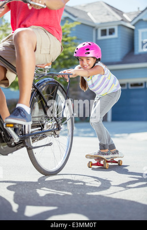 Tochter auf Skateboard Vater auf dem Fahrrad schieben Stockfoto