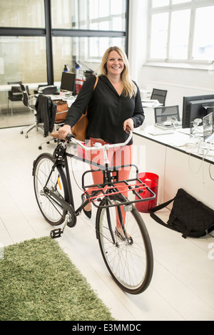 Porträt der Geschäftsfrau mit dem Fahrrad, zu Fuß in Kreativbüro Stockfoto
