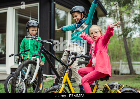 Porträt eines Mädchens mit Armen ausgestreckt Reiten Fahrrad mit Brüdern in Rasen Stockfoto