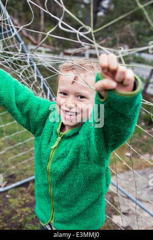 Porträt von fröhlicher Junge hält Fußballnetz in Hof Stockfoto