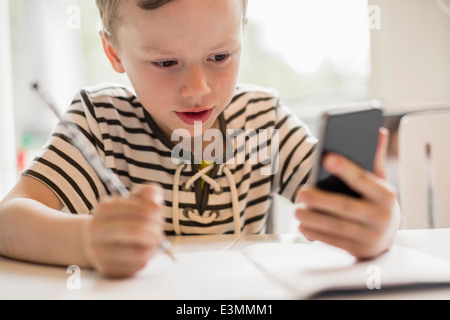 Junge mit Smartphone während des Schreibens am Tisch Stockfoto