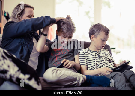 Spielerische Mutter Sohn die Haare neben jungen mit digital-Tablette zu Hause Stockfoto