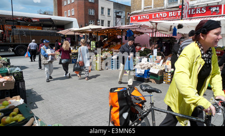 Eine Frau mit einem Fahrrad mit Einkaufen in Packtaschen zu Fuß durch Ridley Road Market, Kingsland Road Dalston East End London E8 UK KATHY DEWITT Stockfoto