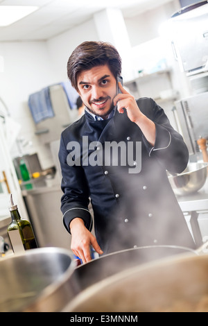 Professionelle Köchin oder Koch in einheitlichen stehend mit einem Edelstahl-Rührschüssel in der Hand, nehmen einen Anruf auf seinem Smartphone whi Stockfoto