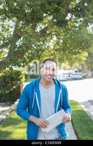 Porträt von lächelnden Mann mit Zeitung auf Bürgersteig Stockfoto