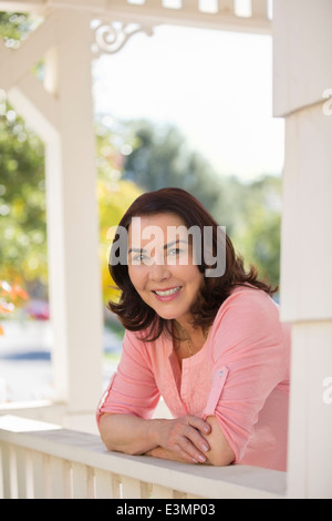 Porträt der lächelnde Frau stützte sich auf Veranda Geländer Stockfoto