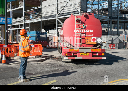 Ein Banksman auf einer britischen Baustelle tragen persönlicher Schutzausrüstung sicher Regie ein Tankwagen Lieferung Stockfoto