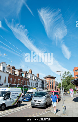 Feder wie Cirrus Wolkenformationen in einem azurblauen Sommerhimmel über eine typisch britische Straßenszene Stockfoto