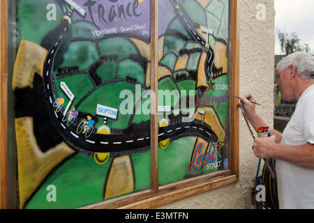 Fensterkünstler mit mahlstick oder Maulstick im Skipton Yorkshire Dales National Park, Großbritannien. Eddie Ralph, lokaler Künstler, Abschluss seiner Malerei als Yorkshire bereitet sich auf Le Tour de France, Die Radkunstwerk-Route ist mit gelben Bikes und Bannern geschmückt, während sich die Unternehmen für das weltgrößte Radrennen rüsten, das am 5. Und 6. Juli 2014 in der Grafschaft beginnt und Millionen von Fans an die Straßenrand von Yorkshire bringt, um die Champions des Sports anzufeuern. Es wird das erste Mal sein, dass Le Tour den Norden Englands besucht hat, nachdem sie zuvor nur die Südküste und die Hauptstadt besucht hat. Stockfoto