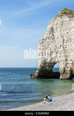 Paar sitzt am Kiesstrand vor dem natürlichen Felsen Bogen Porte d'Amont bei Etretat, Normandie, Frankreich Stockfoto