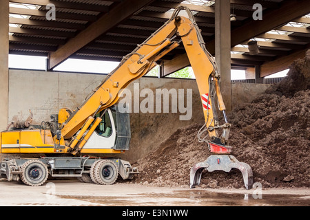 Heavy-Duty-Bagger tun Erdbewegung geparkt in einem offenen Lager vor einem riesigen Haufen von Braunerde für baugewerblicher undercover Stockfoto