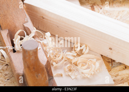 Nahaufnahme eines hölzernen handheld Holz Flugzeug verwendet, um glatte und Ebene Oberfläche ein Holzbrett mit frischen Holzspänen in DIY, Holzbearbeitung, Schreinerei oder Tischlerei Konzept umgeben Stockfoto