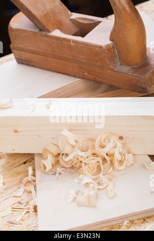 Nahaufnahme eines hölzernen handheld Holz Flugzeug verwendet, um glatte und Ebene Oberfläche ein Holzbrett mit frischem Holz umgeben Stockfoto