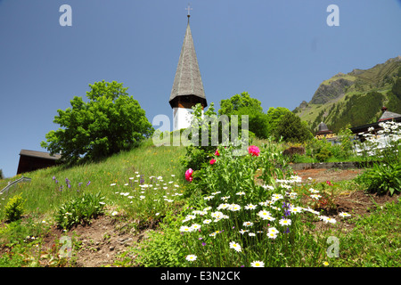 Eine weiße alpine Kirche mit einer Uhr und einem hohen Turm und Blumen. Stockfoto