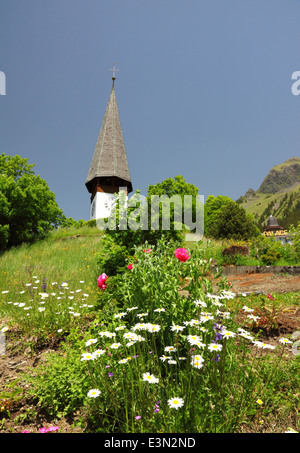 Eine weiße alpine Kirche mit einer Uhr und einem hohen Turm und Blumen. Stockfoto