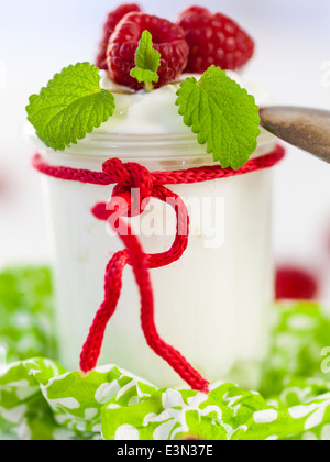 Frische reife Himbeeren serviert mit einem Glas des gesunden Joghurt oder Clotted Cream für ein leckeres Dessert oder Frühstück mit Exemplar Stockfoto