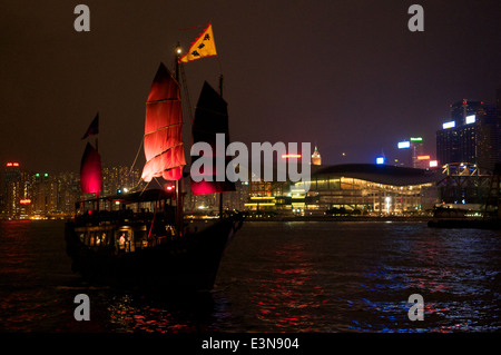 Die legendäre chinesische rote Segel Junk im Victoria Harbour in der Nacht fährt vorbei an das Hong Kong Convention & Exhibition Center, Hong Kong Stockfoto