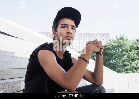 Nachdenklicher junger Mann mit Händen umklammert auf Schritte im Freien sitzen Stockfoto