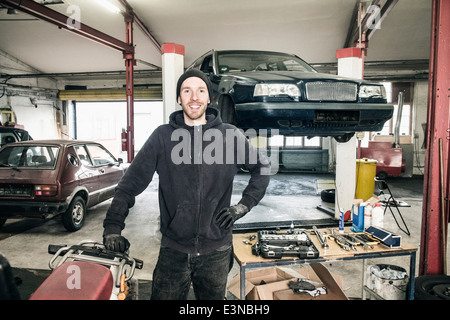Porträt von zuversichtlich männlichen Auto Mechaniker stehend mit der Hand auf die Hüfte in Werkstatt Stockfoto
