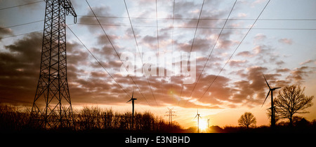 Strommasten und Windräder gegen bewölktem Himmel in der Abenddämmerung Stockfoto