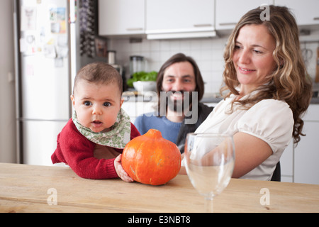 Eltern mit Baby Girl holding Kürbis am Tisch in der Küche Stockfoto