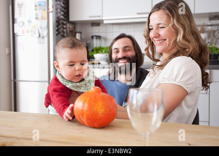 Glückliche Eltern betrachten Babymädchen spielen mit Kürbis in Küche Stockfoto