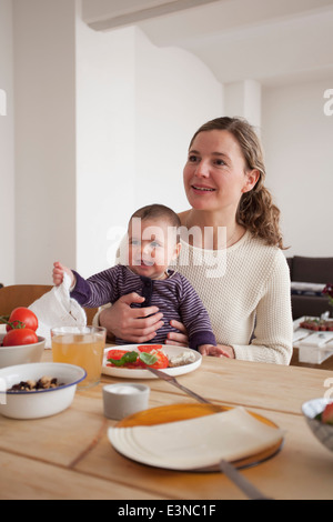 Lächelnde Mutter und Baby Mädchen wegsehen beim Sitzen am Tisch Stockfoto