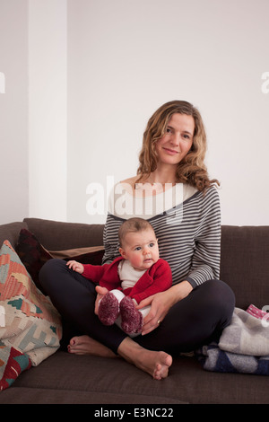 Porträt von Mitte Erwachsene Frau mit Baby Girl auf Sofa zu Hause sitzen Stockfoto