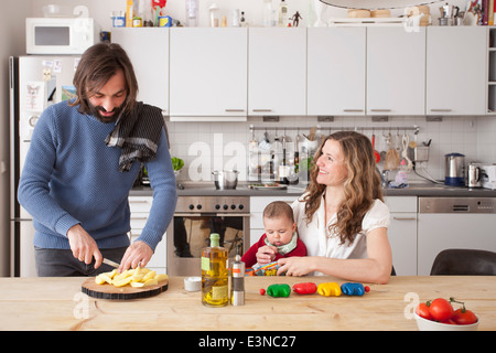 Vater Hacken Gemüse mit Frau und Baby Mädchen sitzen in der Küche Stockfoto