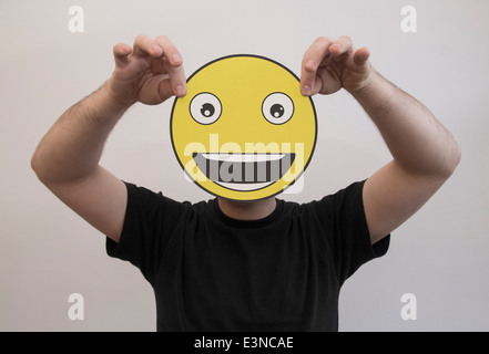 Mann, der ein wirklich glücklich Emoticon Gesicht vor sein Gesicht hält Stockfoto