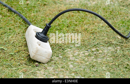 Alte weiße Kunststoff-Adapter Stecker Verlängerungskabel auf dem Boden im Garten. Stockfoto