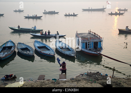 Mann Waschen von Kleidern und touristische Boote am wunderschönen Sonnenaufgang am frühen Morgen in der Nähe von Dhobi Ghat am Ganges in Varanasi, Indien. Stockfoto