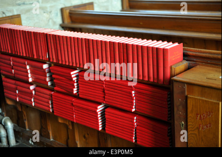 Gesangbücher gestapelt am Ende der Kirchenbank in der Kirche Stockfoto